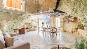 A spacious interior with a high ceiling, stone walls, a dining area, and a large window. - Pleasant Stone House & Jacuzzi St Martin (Mgarr)