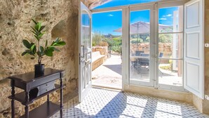 A room with a stone wall, a potted plant, a wooden table, and a view through glass doors to an outdoor patio. - Pleasant Stone House & Jacuzzi St Martin (Mgarr)
