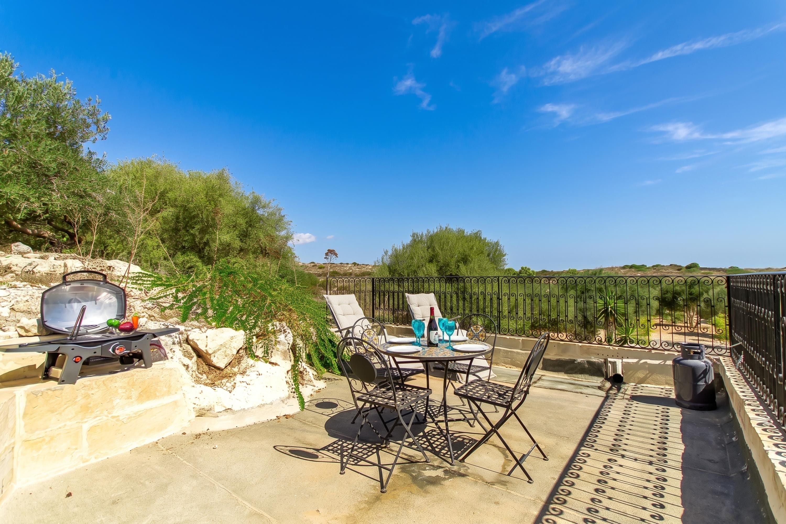 Eine Terrassengruppe im Freien mit Tisch, Stühlen, einem Grill und Blick ins Grüne.