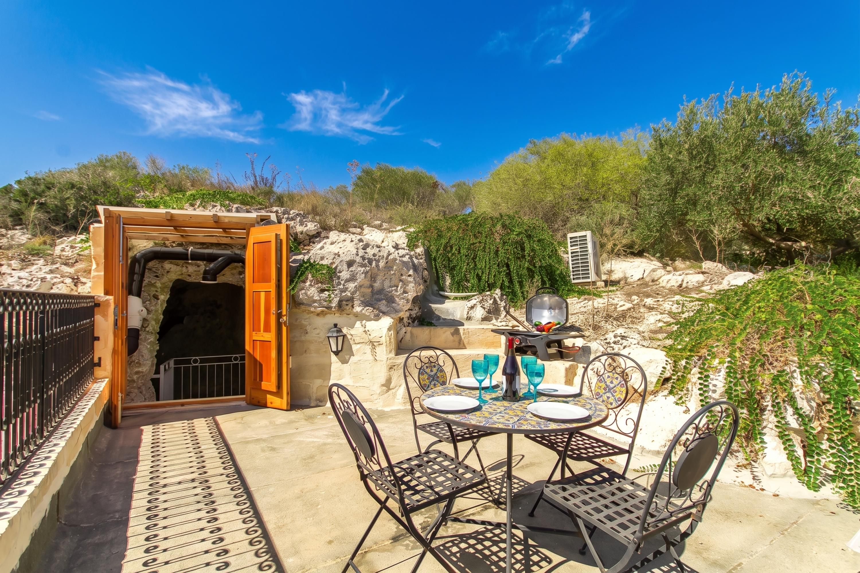 Un patio al aire libre con una mesa lista para comer, una parrilla y vistas del paisaje circundante.
