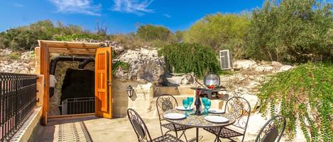 An outdoor patio with a table set for dining, a grill, and a view of the surrounding landscape.