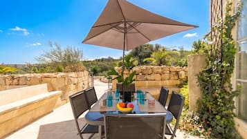 An outdoor dining area with a table, chairs, a large umbrella, and a fruit bowl.