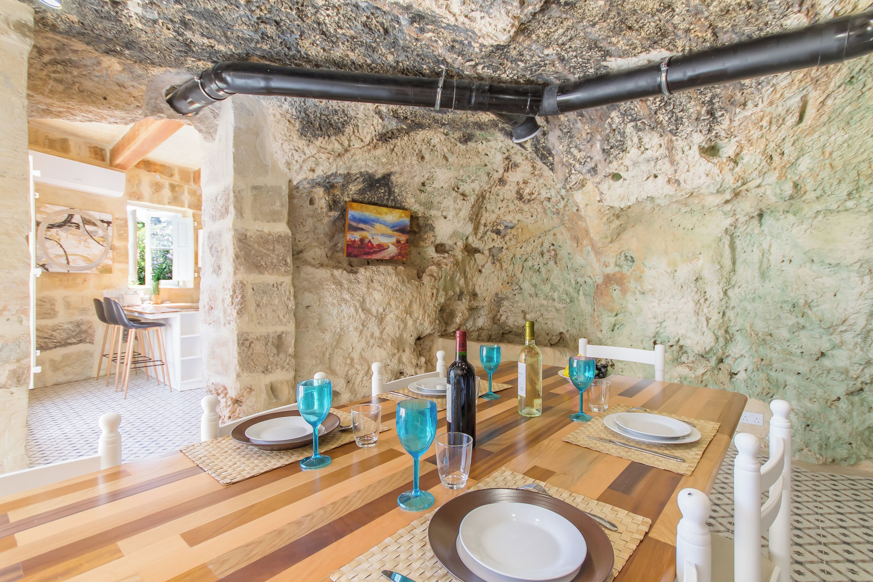 Un comedor rústico con pared de piedra, mesa de madera y cristalería azul.