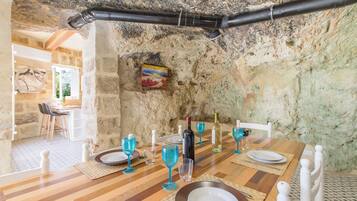 Un comedor rústico con pared de piedra, mesa de madera y cristalería azul.
