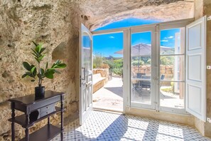 A room with a stone wall, a potted plant, a wooden table, and a view through glass doors to an outdoor patio.