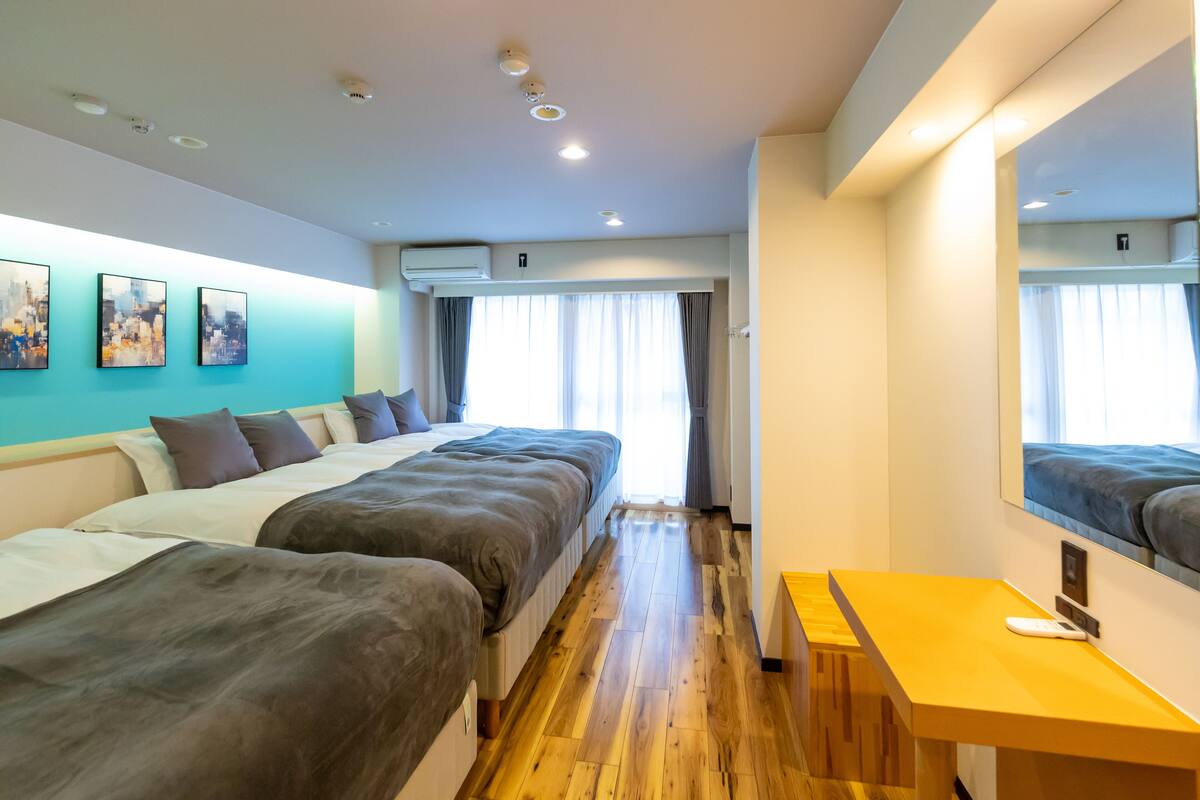 Habitación de hotel con dos camas, piso de madera, un escritorio con computadora y un espejo grande.