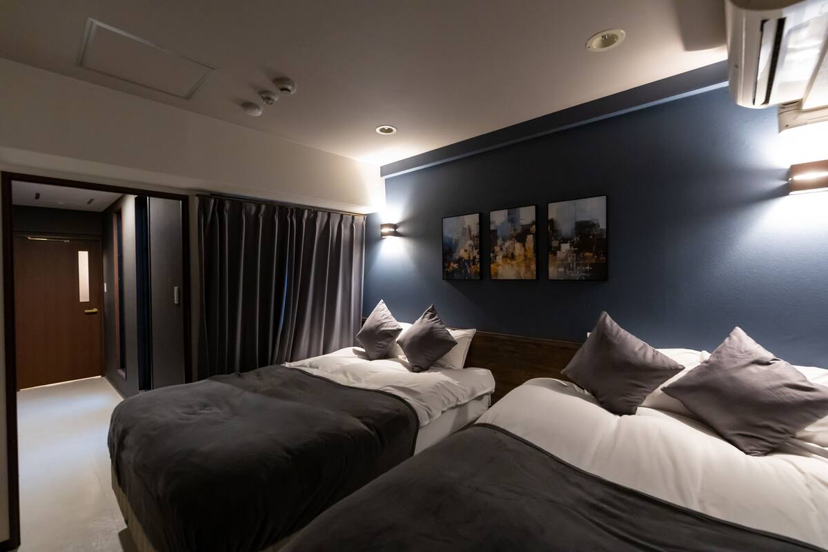 Habitación de hotel con dos camas, una pared de acento azul oscuro y una obra de arte con vista a la ciudad.