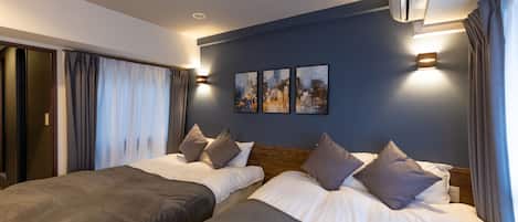 A hotel room with two beds, a cityscape artwork on the wall, and a ceiling-mounted air conditioner.