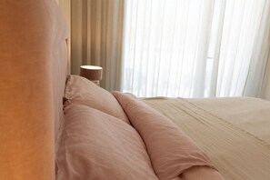A hotel room with a bed, pillows, a nightstand, and a lamp.