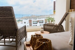 A balcony with wicker furniture, a small table, and a view of buildings in the distance.