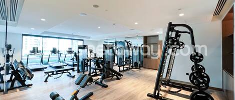 Une salle de sport moderne équipée de divers appareils d’exercice, dotée de grandes fenêtres et d’un plancher en bois.