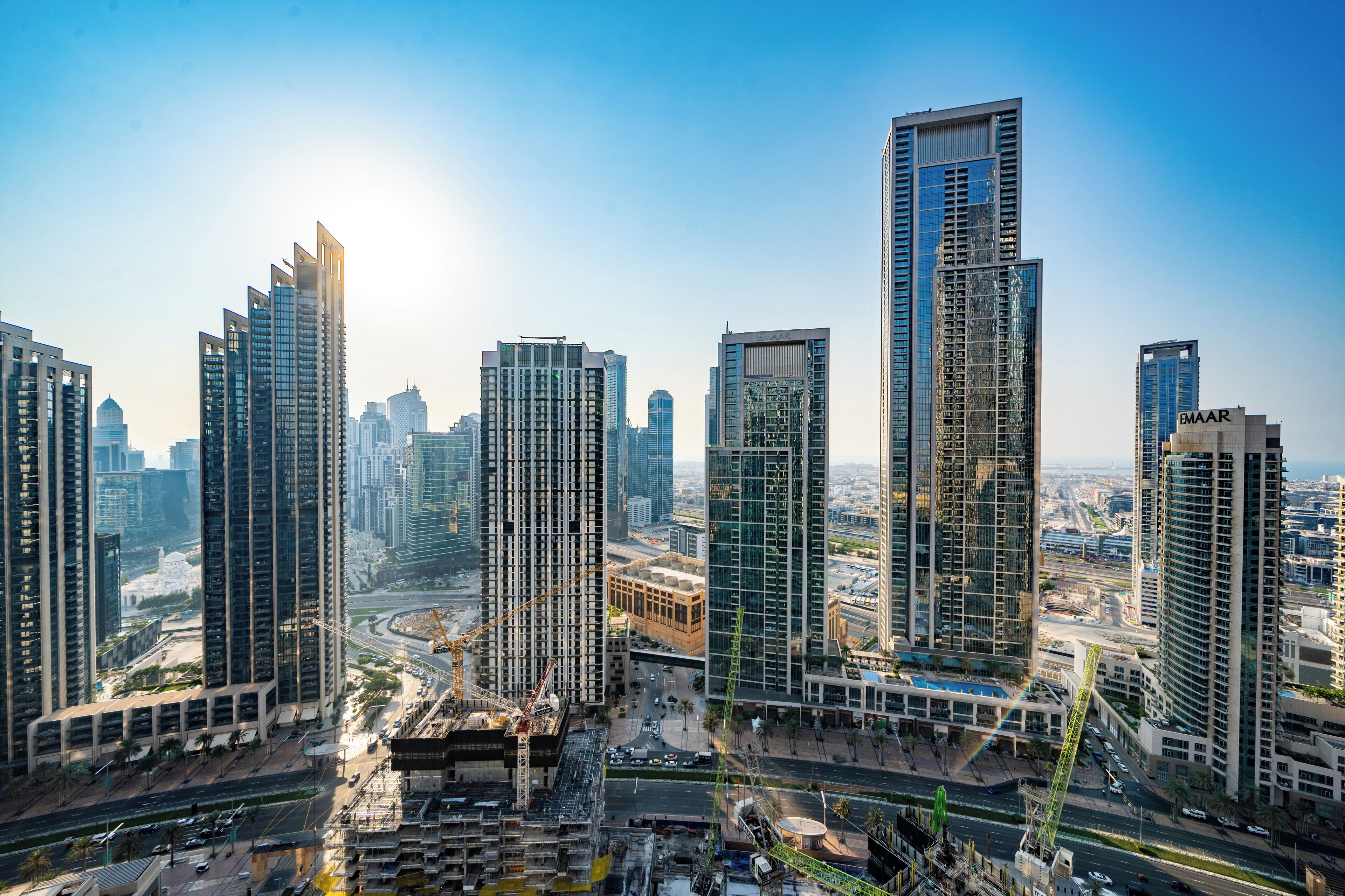 A high-rise urban area with modern skyscrapers, a busy road, and construction cranes.