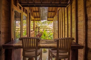 Una habitación de madera con una mesa y sillas, y vistas a un jardín con plantas y una palmera.