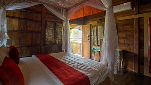 Una habitación de madera con una cama, una mesita y una puerta que da al exterior.