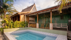 Una piscina con mosaicos, una terraza de madera y una casa tradicional con tejado de baldosas.