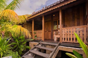 Una casa de madera con un porche, escalones que llevan a la entrada y plantas tropicales alrededor.