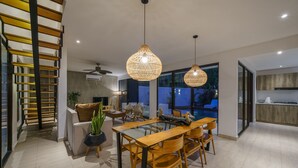 Uma área de jantar moderna com mesa de vidro e cadeiras de madeira, um ventilador de teto e uma janela grande com vista para o exterior.