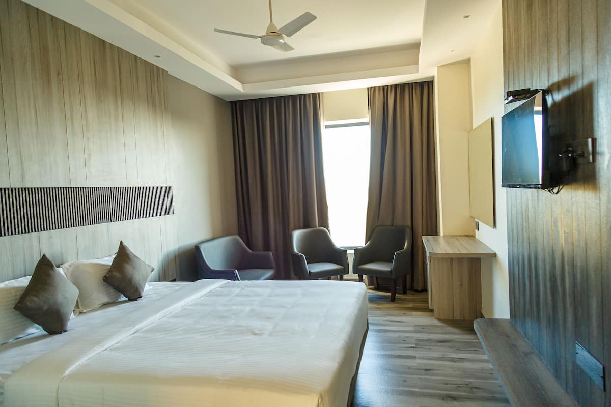 A hotel room with a large bed, two armchairs, a small table, a TV, and a ceiling fan.