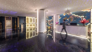 A modern lobby with a reflective floor, a reception desk, and a decorative wall with lights.