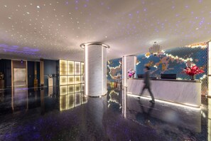 Een moderne lobby met een spiegelende vloer, een receptiebalie en een decoratieve wand met verlichting.