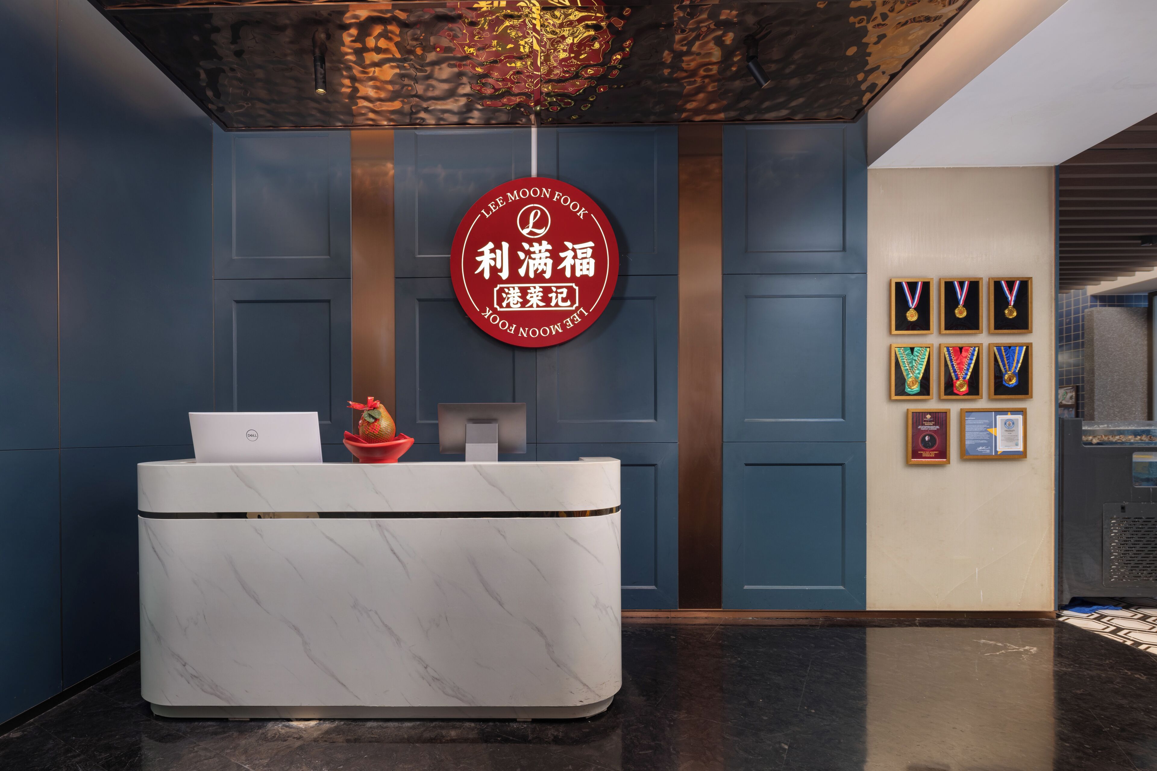 Un comptoir d’accueil avec un ordinateur portable, un saladier décoratif rempli de fruits et un panneau circulaire rouge orné de caractères chinois.
