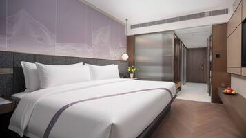 A modern hotel room with a large bed, a nightstand, a wall-mounted TV, and a bathroom visible through a sliding door.
