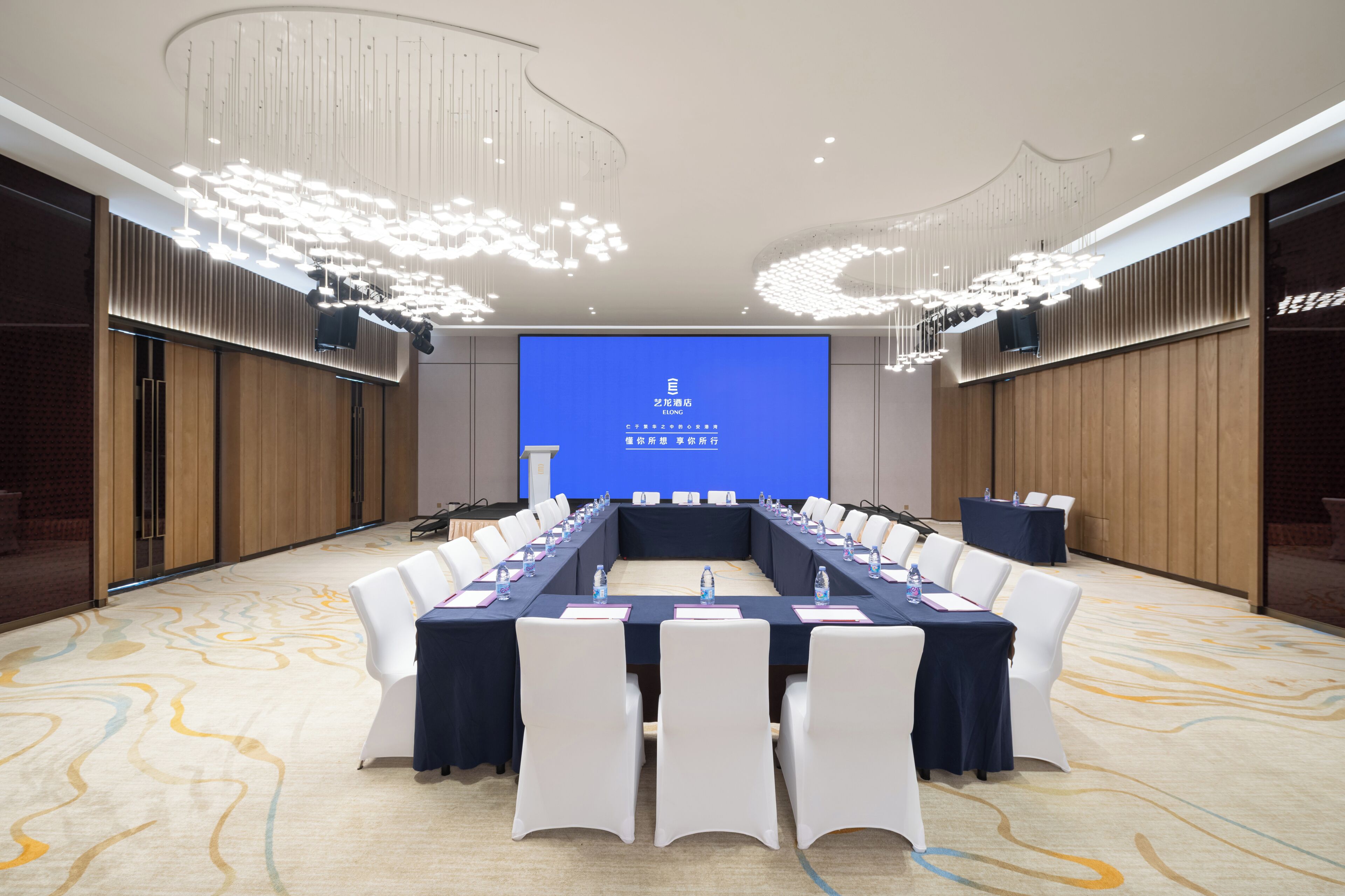 A conference room with a long table, white chairs, and a large screen displaying text.