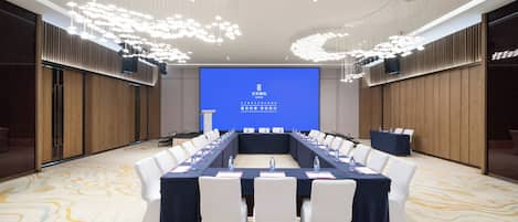 A conference room with a long table, white chairs, and a large screen displaying text.