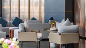 A modern lounge area with sofas and armchairs, a round table with a vase, and large windows with a view.