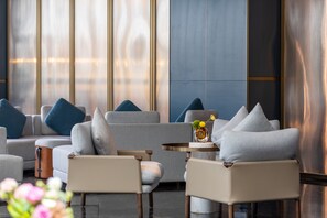 Een moderne lounge met banken en fauteuils, een ronde tafel met een vaas, en grote ramen met uitzicht.
