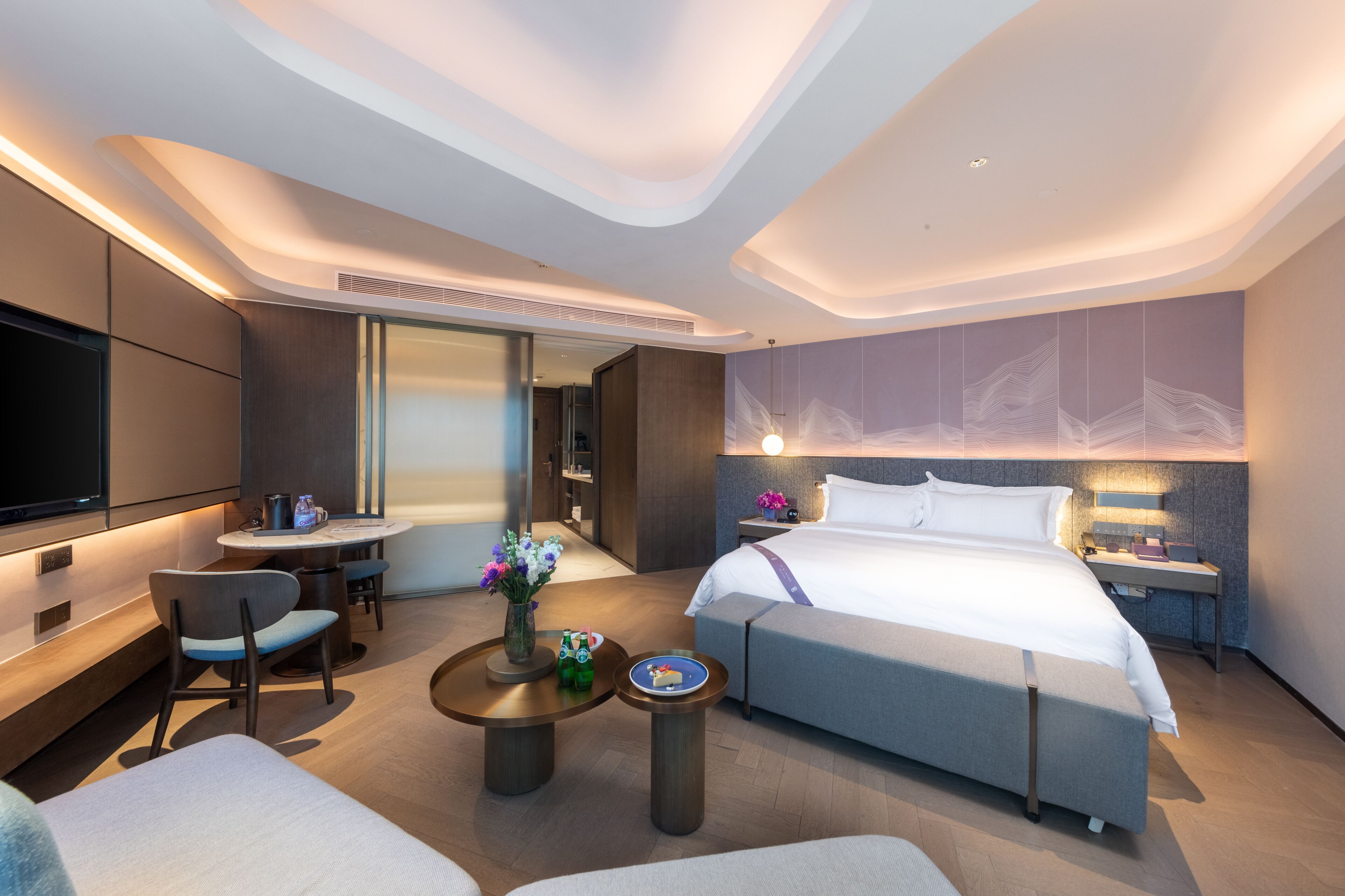 Ein modernes Hotelzimmer mit einem großen Bett, einem Schreibtisch, einem Fernseher und einer Sitzecke mit Stühlen und einem Tisch.