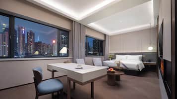 A modern hotel room with a city view, a dining area, and a bed with a nightstand.