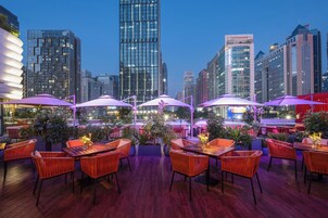 An outdoor seating area with tables and chairs, surrounded by city buildings.