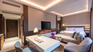 Una habitación de hotel moderna con televisión de pantalla plana, chimenea, cama, escritorio con lámpara y zona de estar.