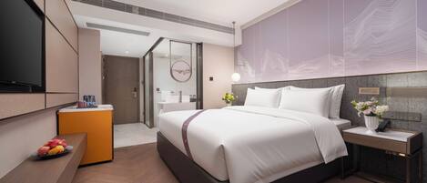 Una habitación de hotel moderna con una cama grande, un escritorio, un televisor y un baño visible a través de una puerta abierta.