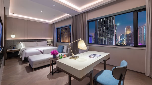 Una habitación de hotel moderna con cama, mesita de noche, lámpara y escritorio con silla.