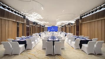 A conference room with rows of tables and chairs, a large screen at the front, and modern lighting fixtures.