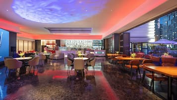 A modern bar area with a ceiling projection, seating arrangements, and a view of the cityscape.