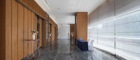 A modern hotel corridor with wooden paneling, marble flooring, and glass partitions.
