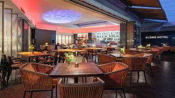 A restaurant with wooden tables and wicker chairs, a bar area, and a ceiling with a light projection.