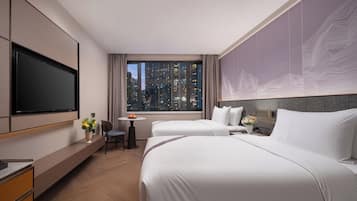 A hotel room with two beds, a desk, a chair, a TV, and a window with a city view.