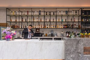 Een bar met een bartender, een marmeren toonbank, flessenrek met drank en een bloemstuk.