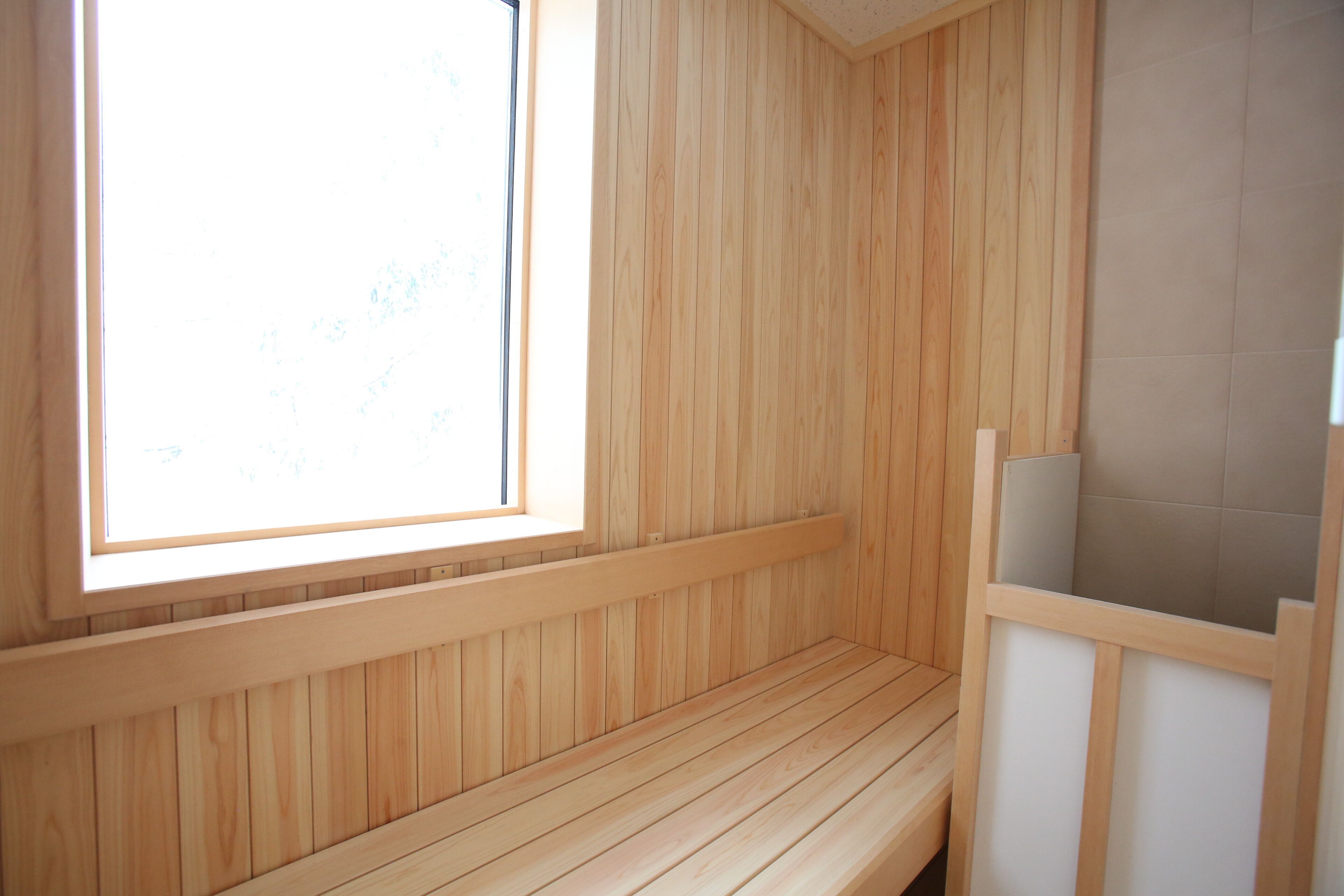 Uma sauna de madeira com um banco, uma janela e uma parede revestida de azulejos.