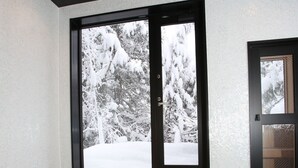 A modern bathroom with a large bathtub, a window with a snowy view, and a door with a frosted glass panel. - Alpine Tenshi Villa (Hakuba)