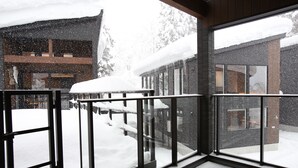 A snow-covered balcony with a view of a building and trees. - Alpine Tenshi Villa (Hakuba)
