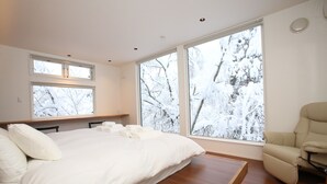 A bedroom with a large bed, a chair, and large windows with a snowy view. - Alpine Tenshi Villa (Hakuba)