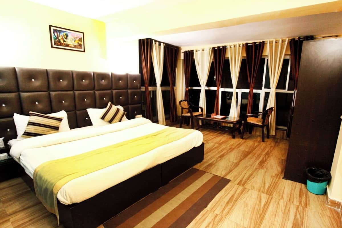 Een hotelkamer met een groot bed, een houten vloer, een raam met gordijnen en een kleine tafel met stoelen.