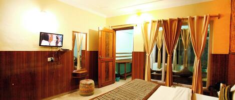 A hotel room with a bed, a television, a mirror, a wardrobe, and curtains.