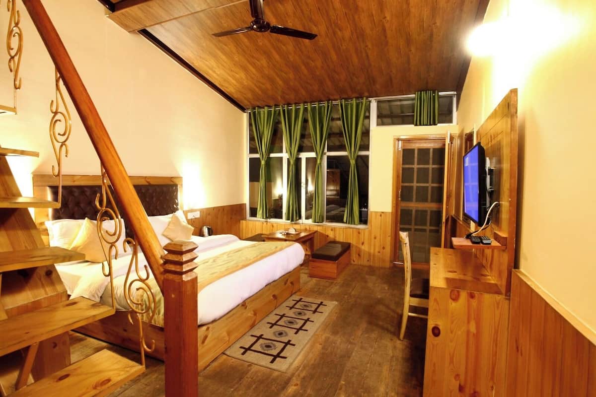 Een houten slaapkamer met een bed, een bureau, een televisie en een raam met gordijnen.