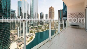 A balcony with a view of a cityscape, including modern high-rise buildings and a body of water. - HomesGetaway- 1BR in JLT Lake Views (Dubai)